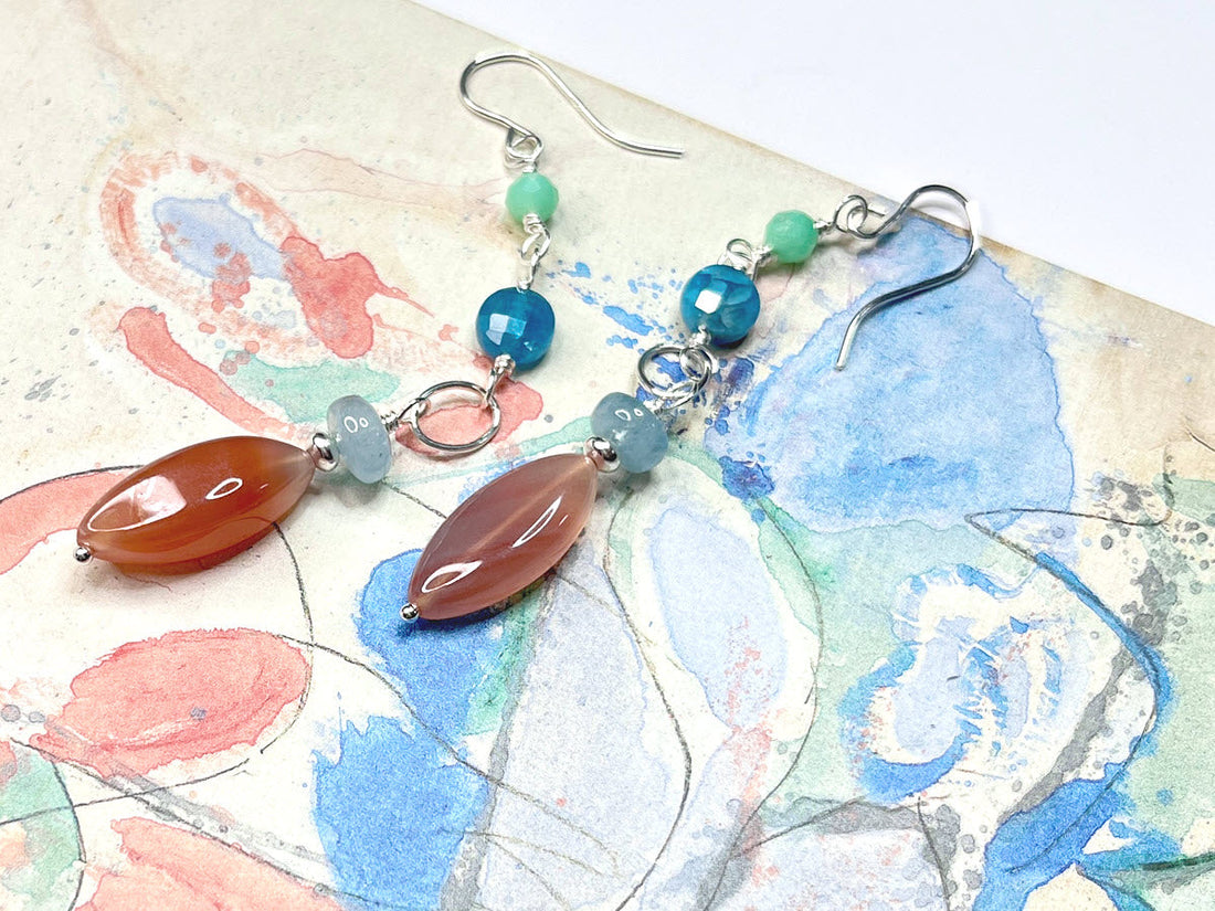 Blue, green and coral-colored dangle earrings on detail of painting