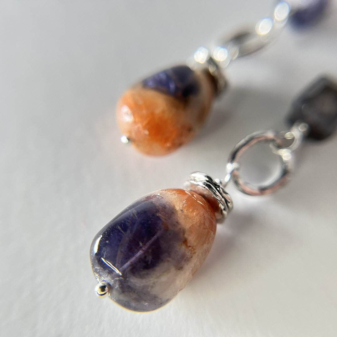 Close-up of a pair of sterling earrings with multicolor combination of iolite and iolite-sunstone tumbled nugget gemstones; long dangles
