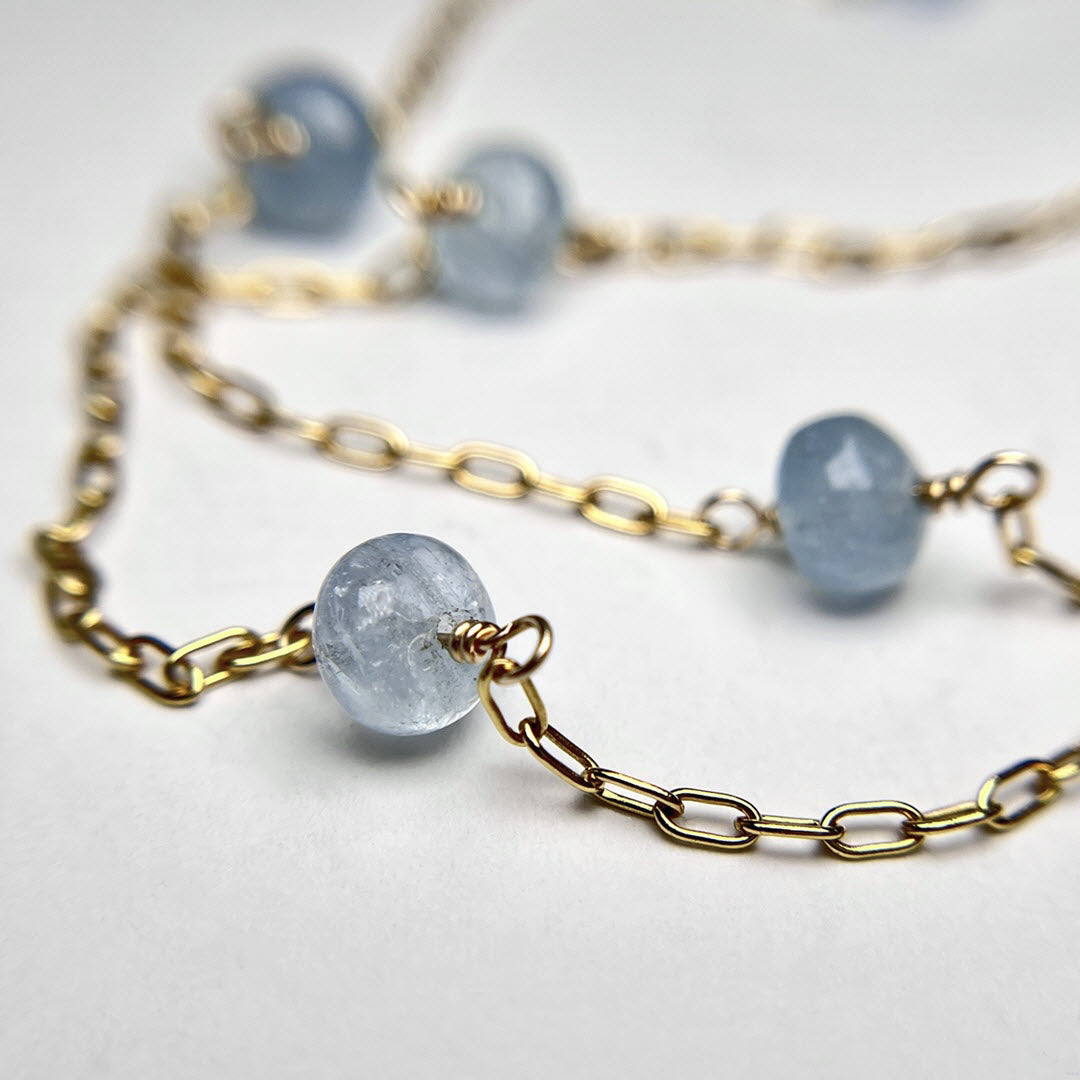 Closeup of Station necklace with 19 light blue aquamarine gemstones on long 14K gold fill chain